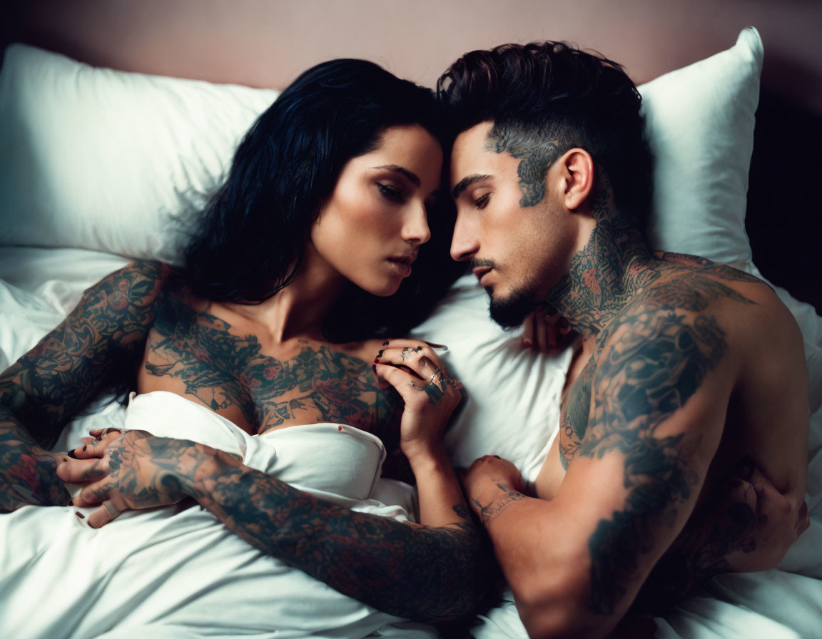 Tattooed couple gazing romantically on bed