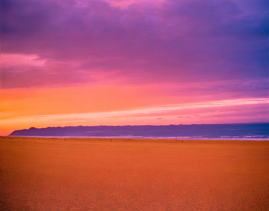 Vivid Sunset Over Sandy Beach with Mountains and Figures