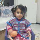 Toddler in colorful outfit sitting by window with cushion and lamp
