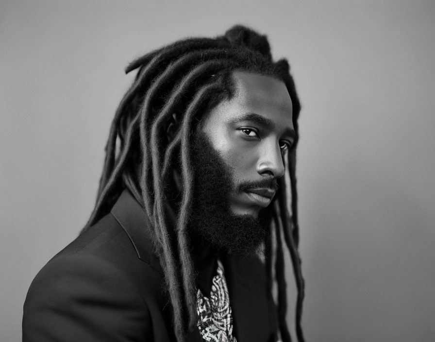 Monochrome portrait of man with long dreadlocks in suit, gazing at camera
