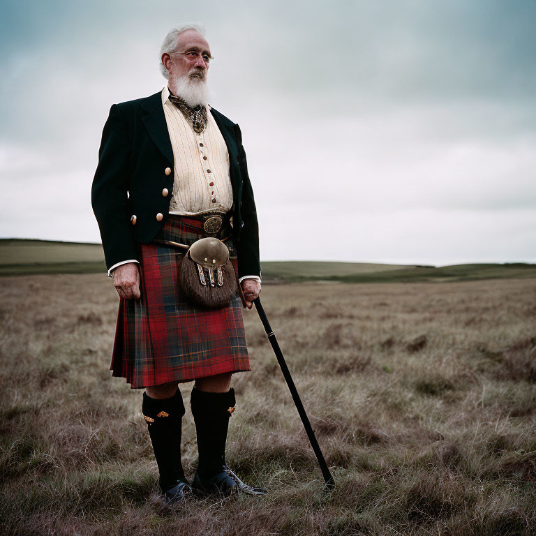 Elderly man in traditional Scottish attire with cane on grassy field