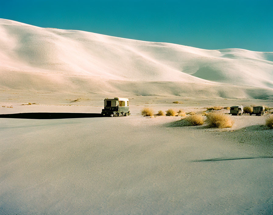 Convoy of vehicles crossing sandy dunes under blue sky