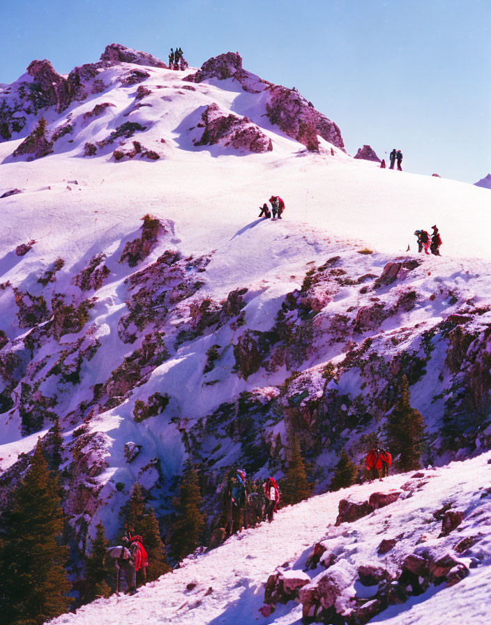 Colorful gear mountaineers ascend steep, snowy slope under clear sky