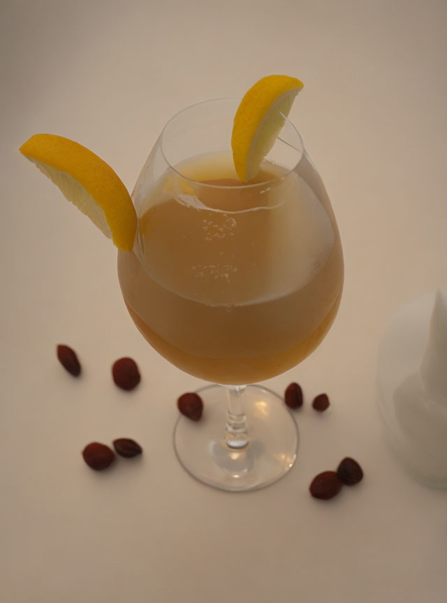 Golden beverage in stemmed glass with lemon slices and almonds on white surface