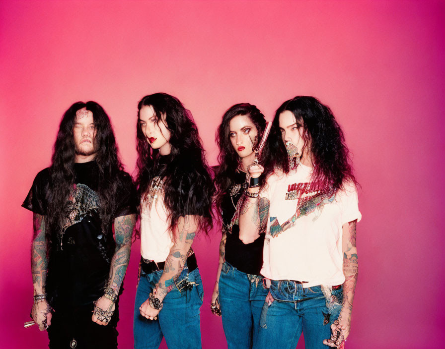 Group of four tattooed individuals posing on pink background in black tops and blue jeans