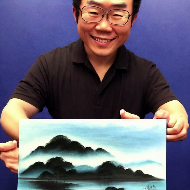 Smiling man with glasses holding landscape painting of misty mountains