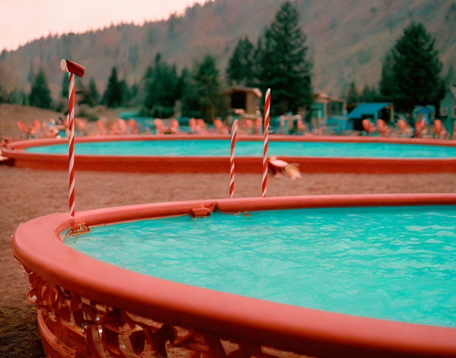 Empty circular kiddie pools with blue water, slides, red accents, trees, and hill view.