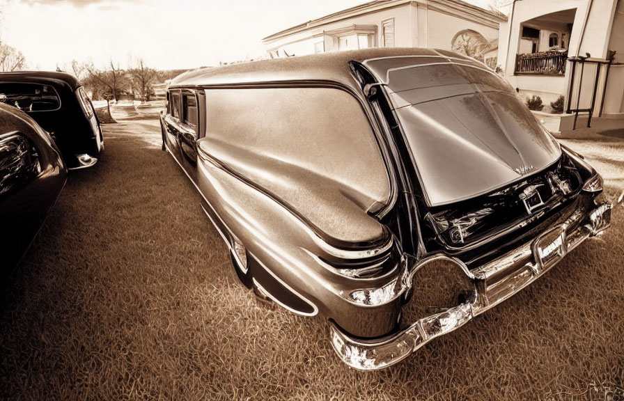 Vintage classic car with tailfin design parked outside residence in sepia tone.
