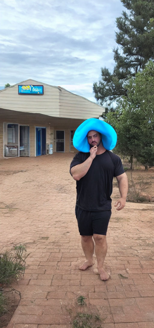 Man in black outfit with blue foam hat outside Village Inn in sandy area