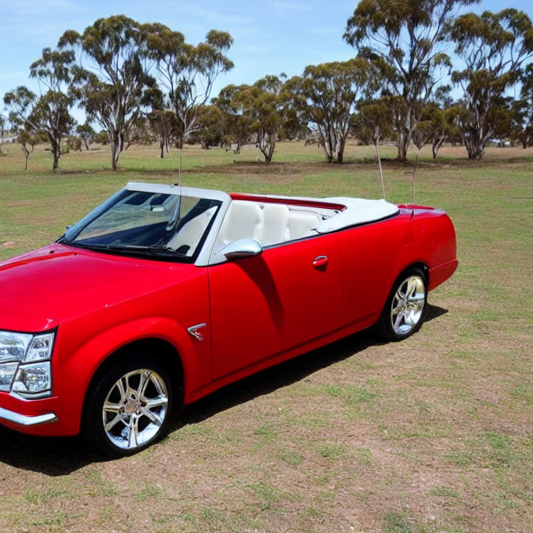 Red Convertible Car Parked with Top Down on Grass Field and Trees Against Blue Sky