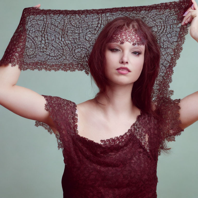 Woman holding lacy fabric against teal background in burgundy lace dress