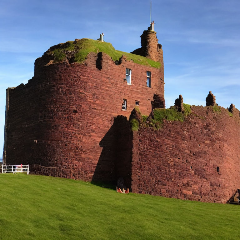 Robust red sandstone castle with battlements on lush green lawn
