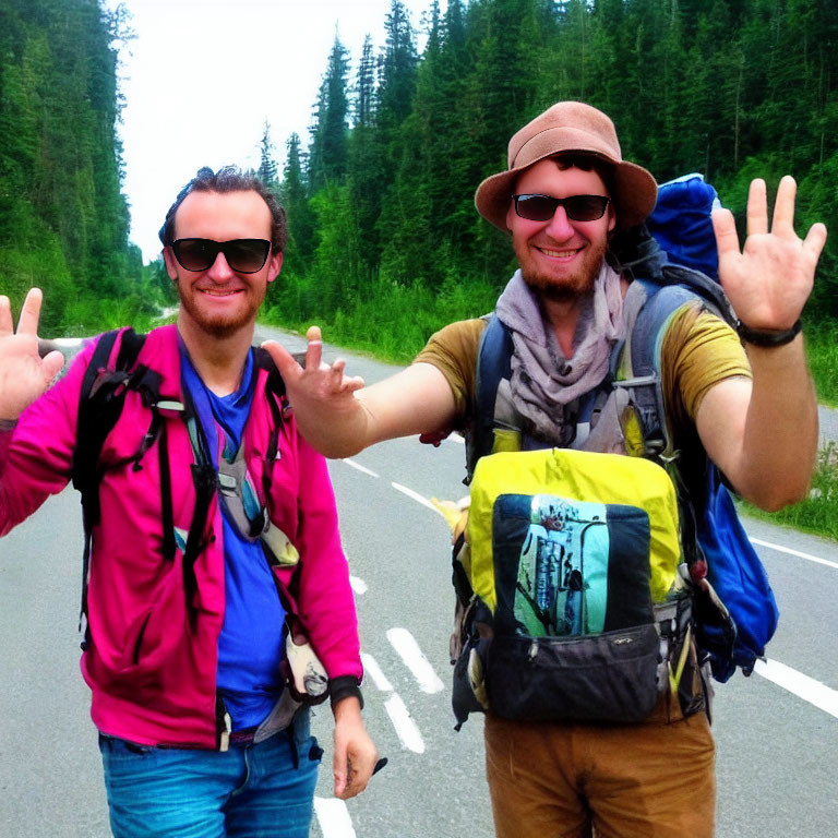 Smiling hikers with backpacks on forest road pose with peace sign