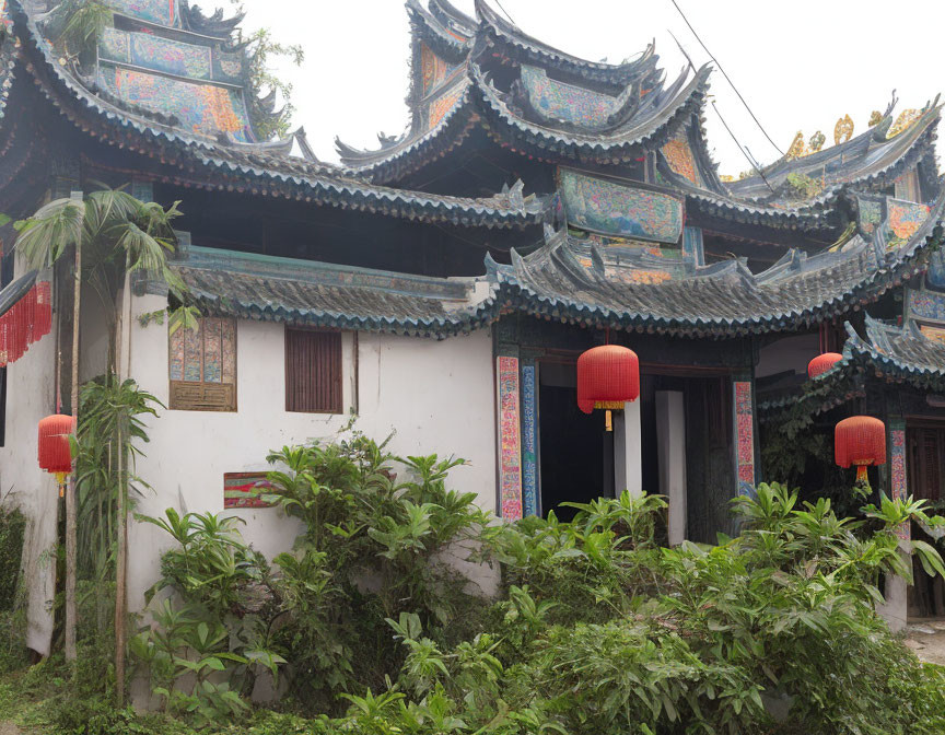 Traditional Chinese architecture with upturned roofs and red lanterns amidst green shrubbery