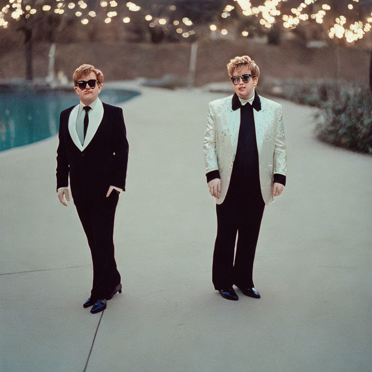 Two flamboyantly dressed individuals by a pool with lights.