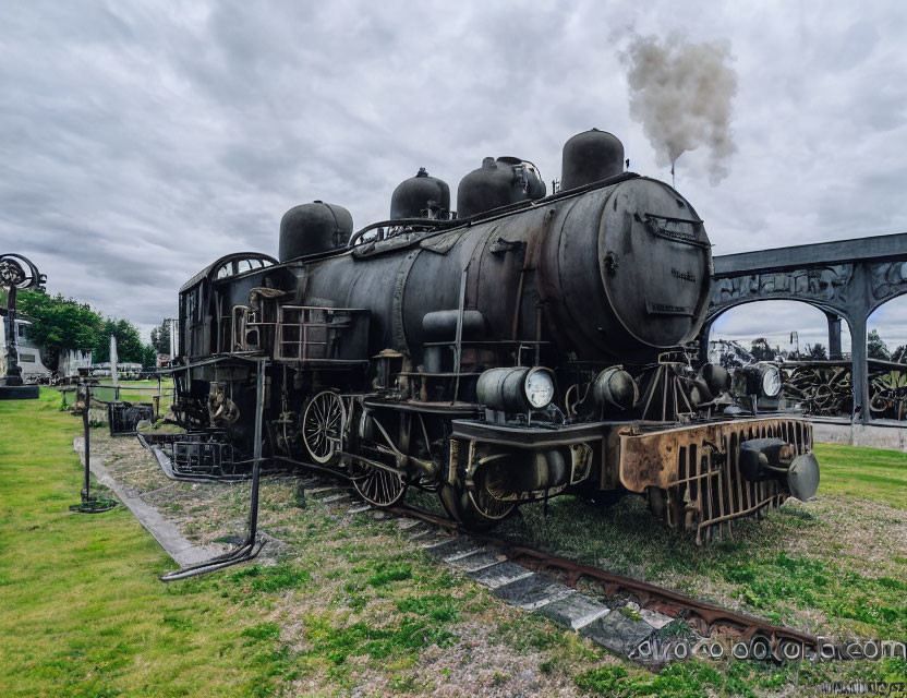 Vintage steam locomotive emitting smoke on outdoor tracks under cloudy skies