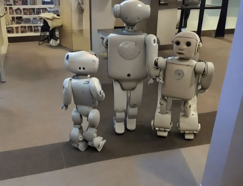 Three humanoid robots of varying sizes in white and gray, set on beige floor.