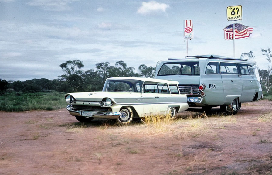 Vintage white and green station wagon and classic green van parked on dusty road with road signs and cloudy sky