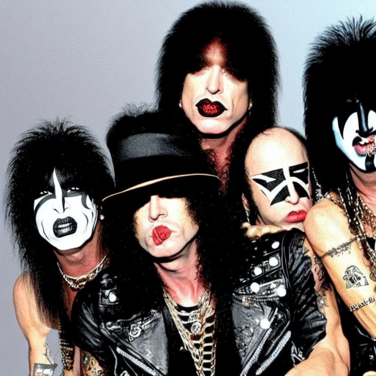 Four individuals in black and white face makeup and rock-style outfits with leather and spikes.