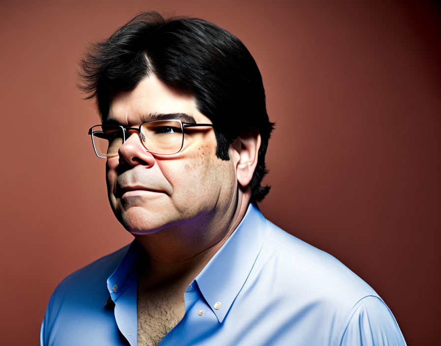 Serious man in blue shirt with black hair and glasses on red background