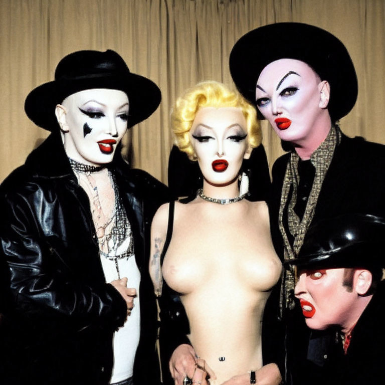 Four individuals in dramatic makeup and costumes with bold lipstick and eye makeup.