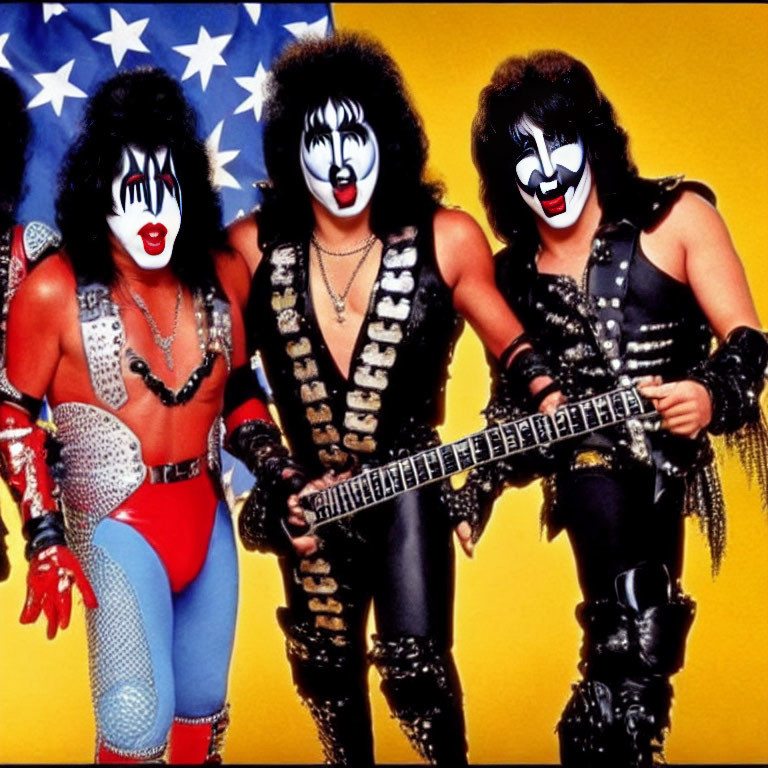 Three individuals in flamboyant costumes with face paint posing with a guitar against an American flag.