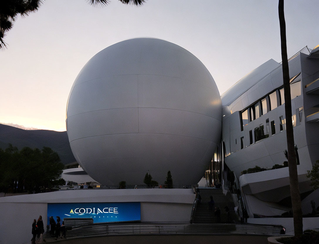Modern building and white spherical structure at dusk with people walking near sign "ACOPIACEE