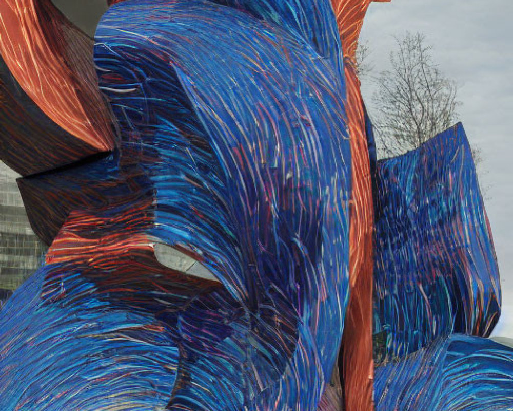 Colorful abstract outdoor sculpture with blue and red swirls among trees and building