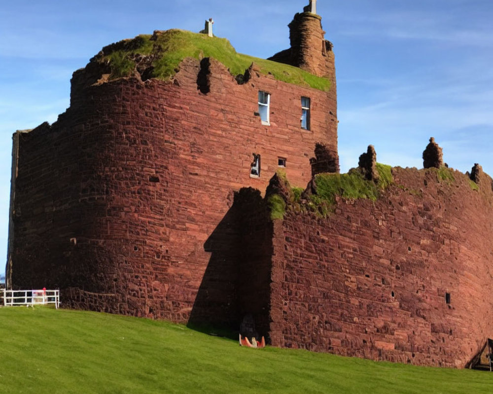 Robust red sandstone castle with battlements on lush green lawn