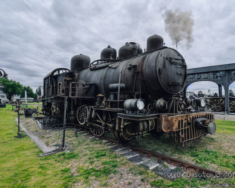 Vintage steam locomotive emitting smoke on outdoor tracks under cloudy skies