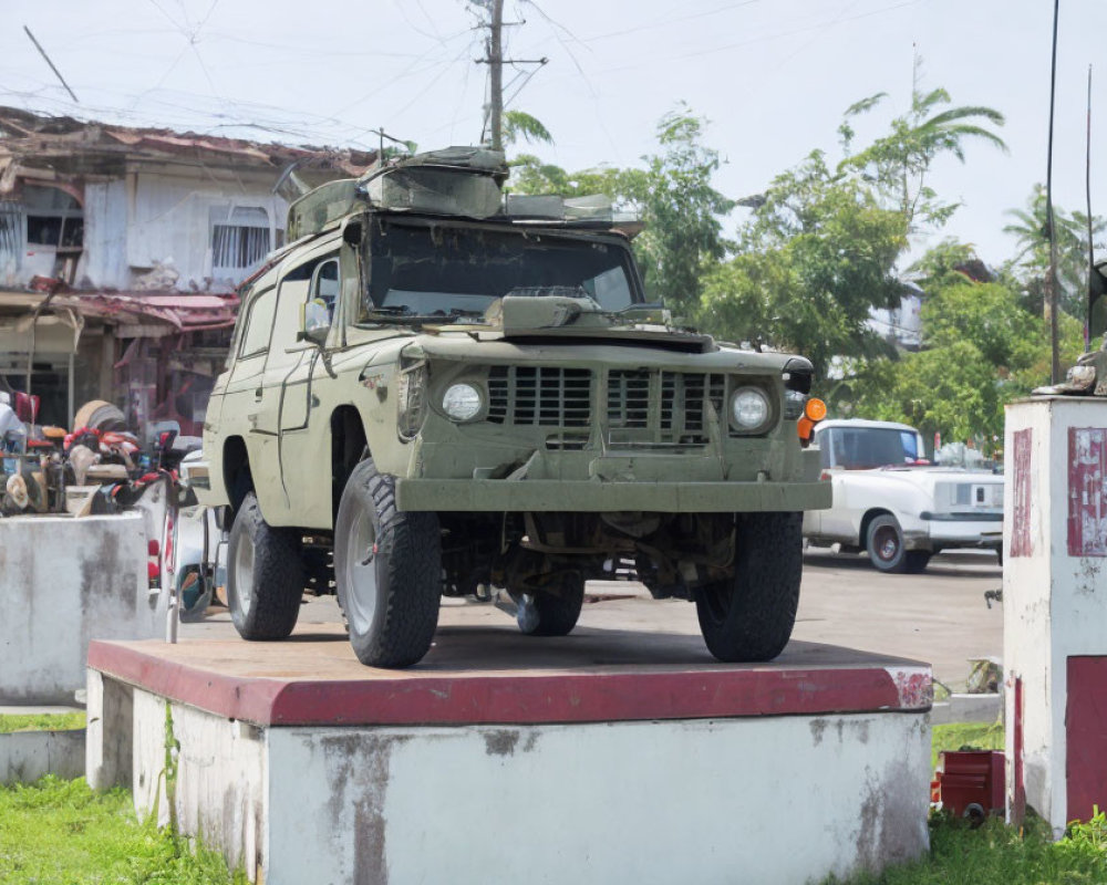Military vehicle with mounted gun parked near street and building, tropical trees in background