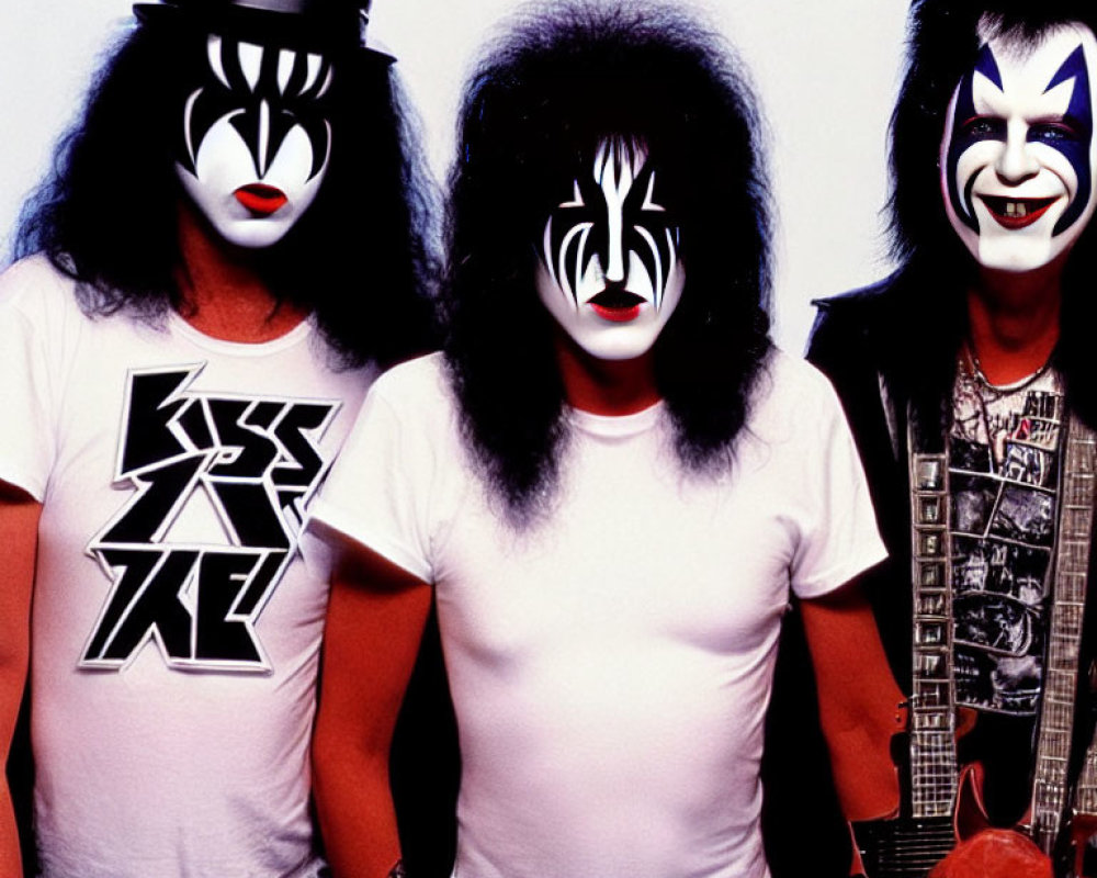 Three individuals in KISS-inspired makeup, black and white attire, two with guitars
