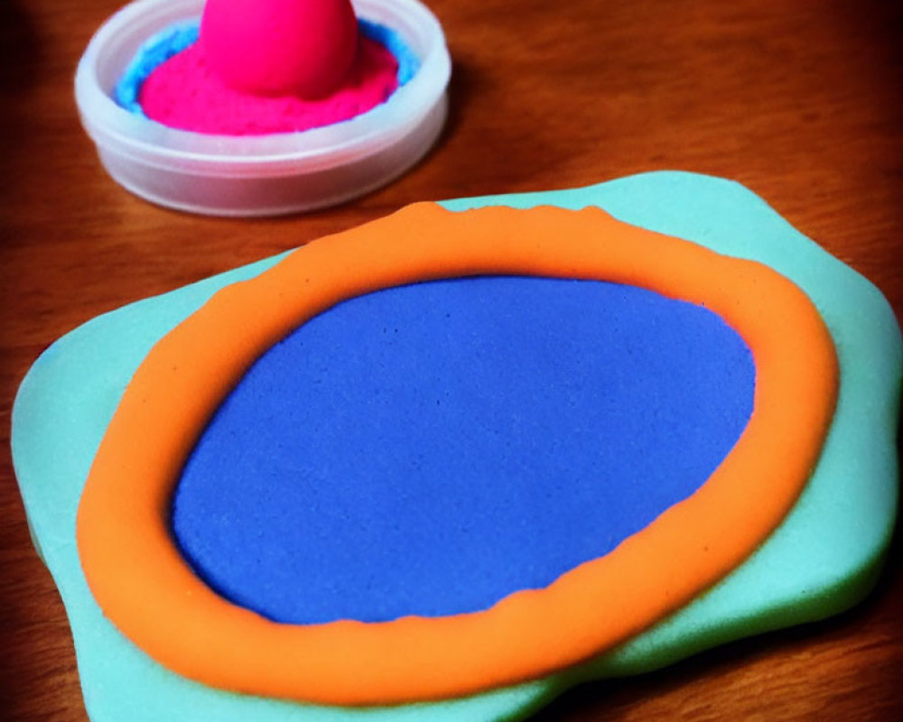 Vibrant playdough art on wooden surface with blue and orange frame shape, pink container,