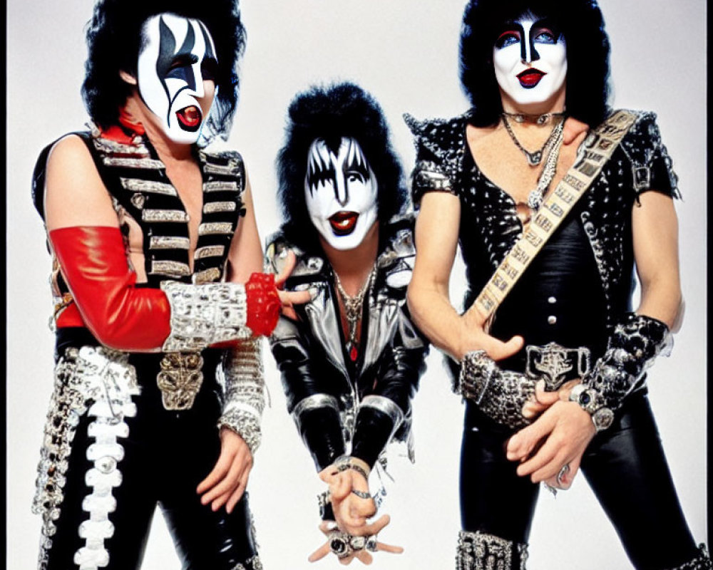 Group of three with black and white face makeup and rock costumes holding instruments