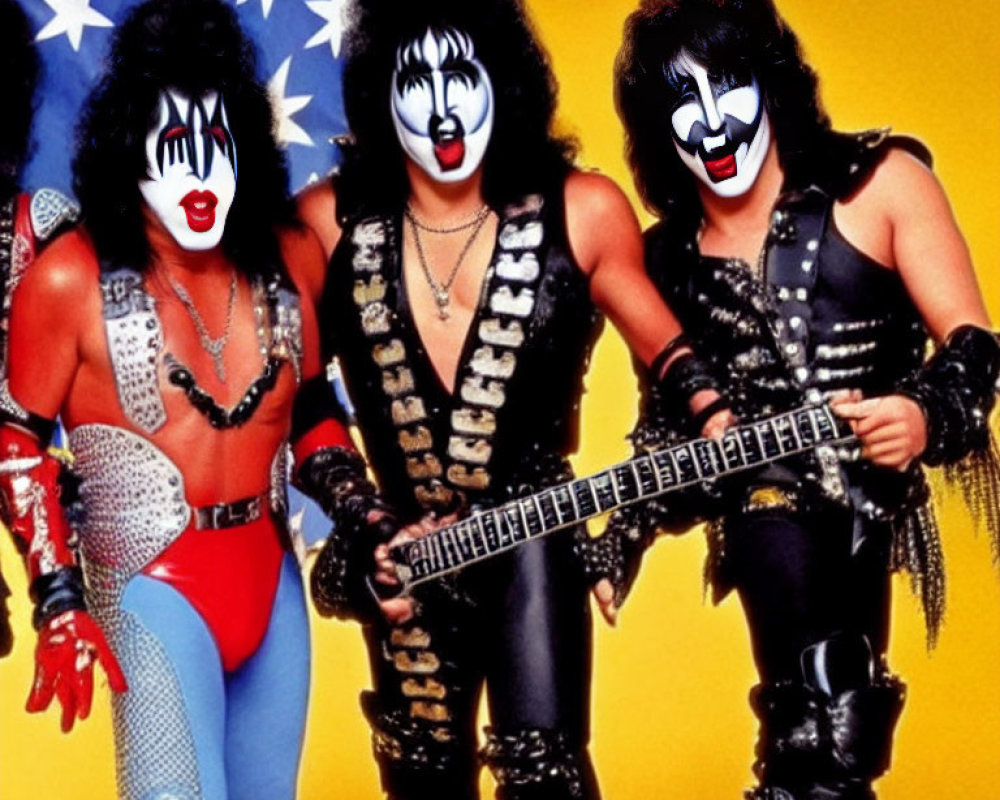 Three individuals in flamboyant costumes with face paint posing with a guitar against an American flag.