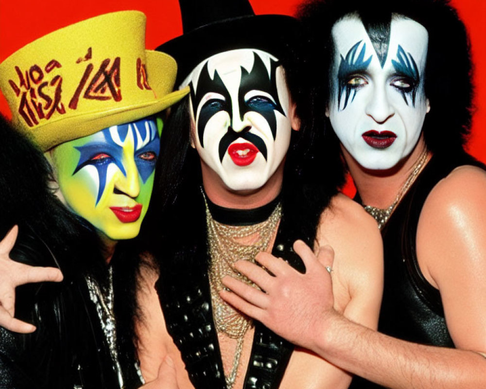 Three individuals in KISS-inspired makeup and costumes on red backdrop