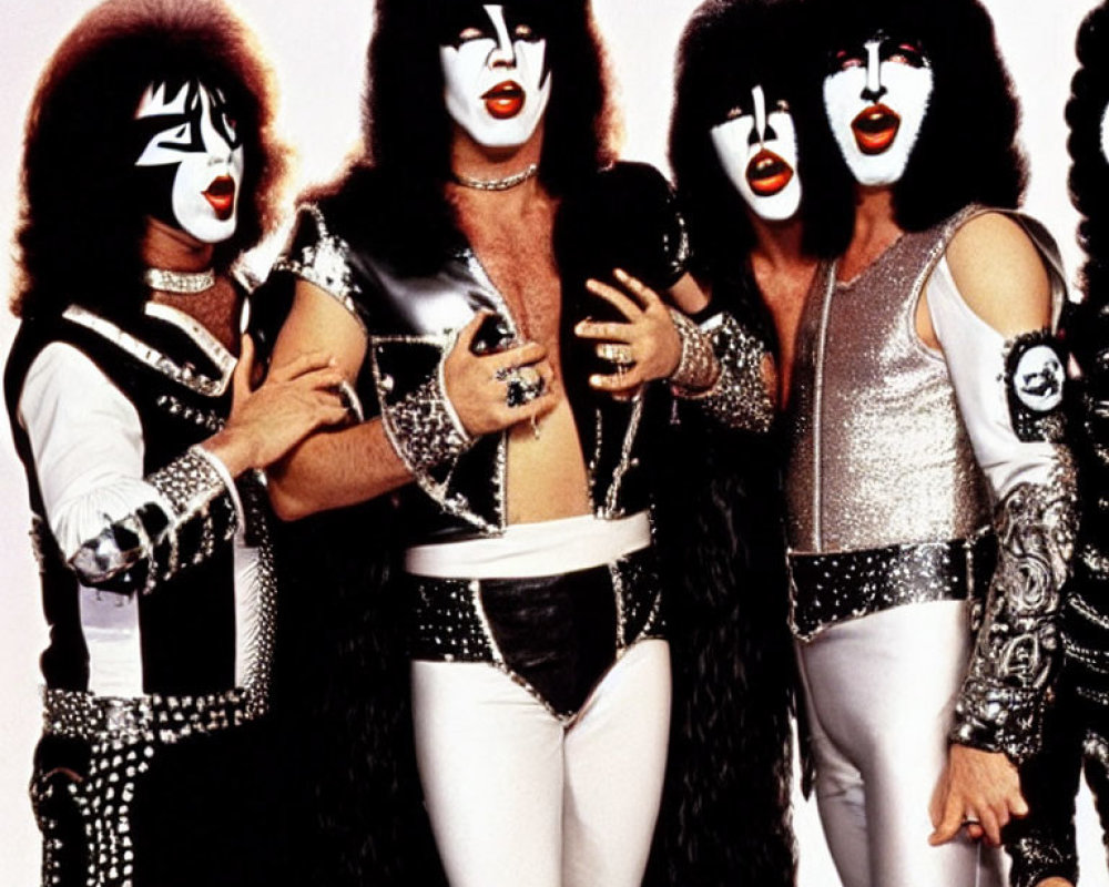 Group of four individuals in glam rock outfits and iconic face paint posing in black and silver costumes