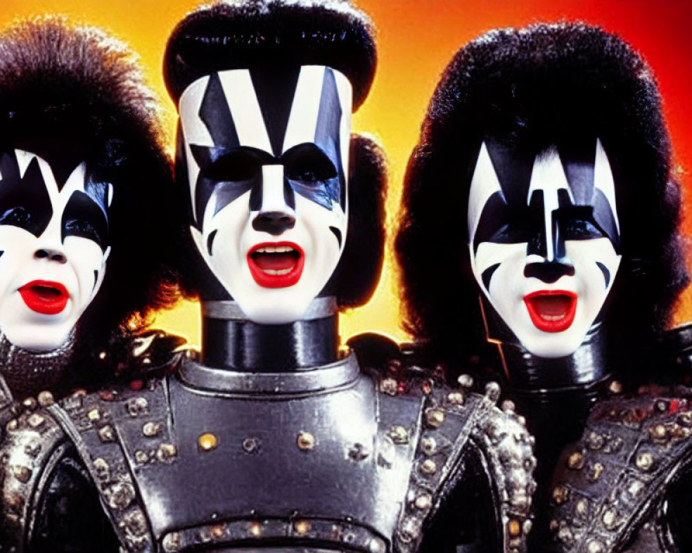 Three individuals in black and white face makeup and flamboyant rock costumes against fiery orange backdrop