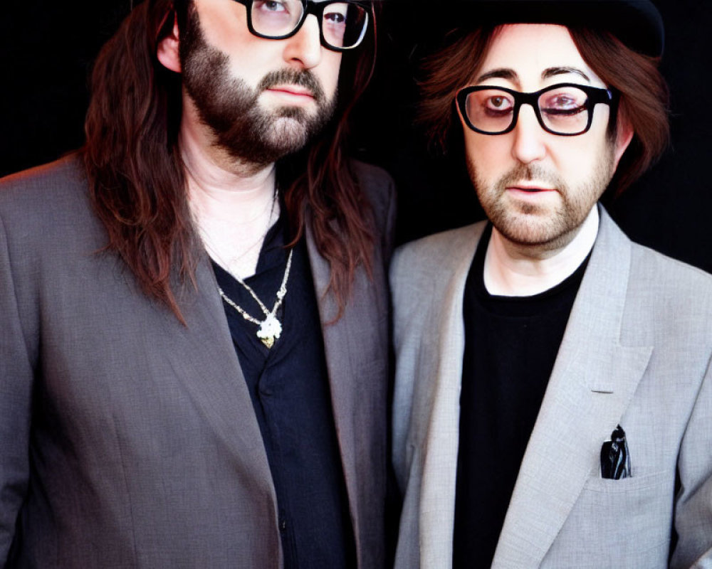 Two men in suits and hats with long hair and glasses standing together.