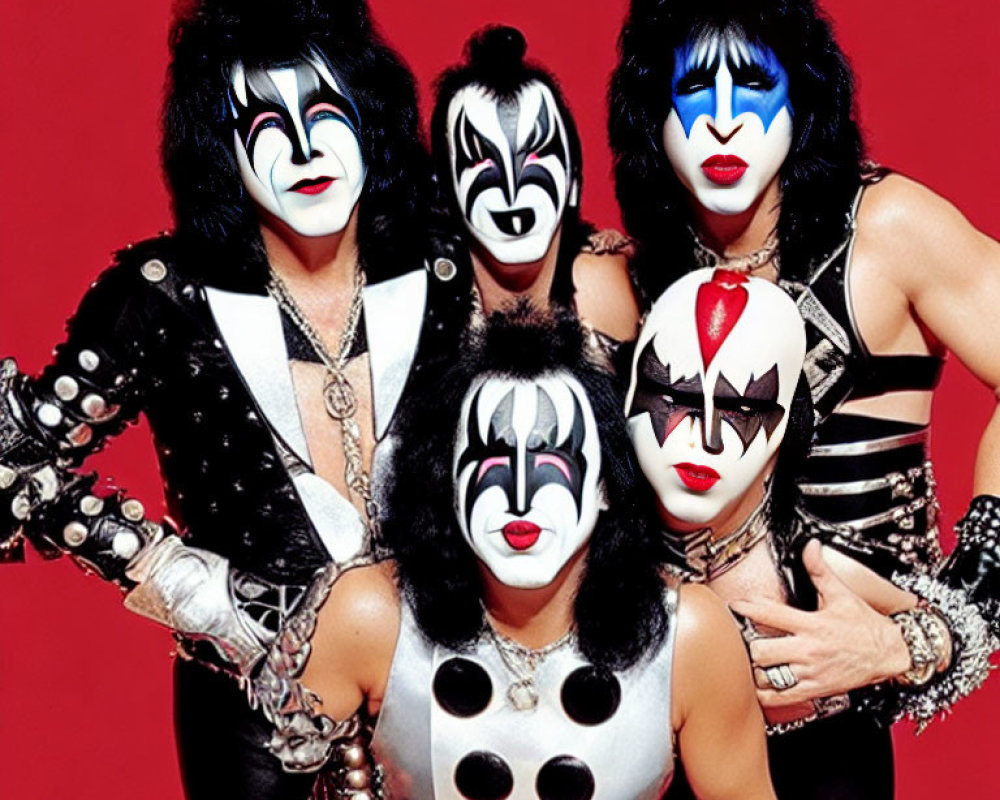 Four individuals in black and white face paint and rock costumes on red background