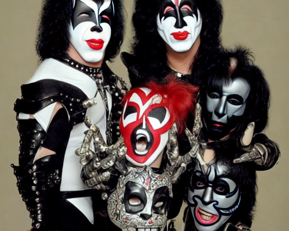 Four individuals in black and white face paint in flamboyant rock band costumes.