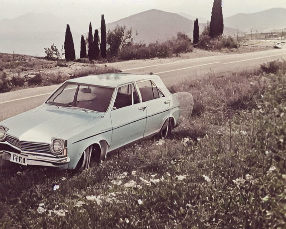 Abandoned vintage blue car in overgrown grass with hills and cloudy sky