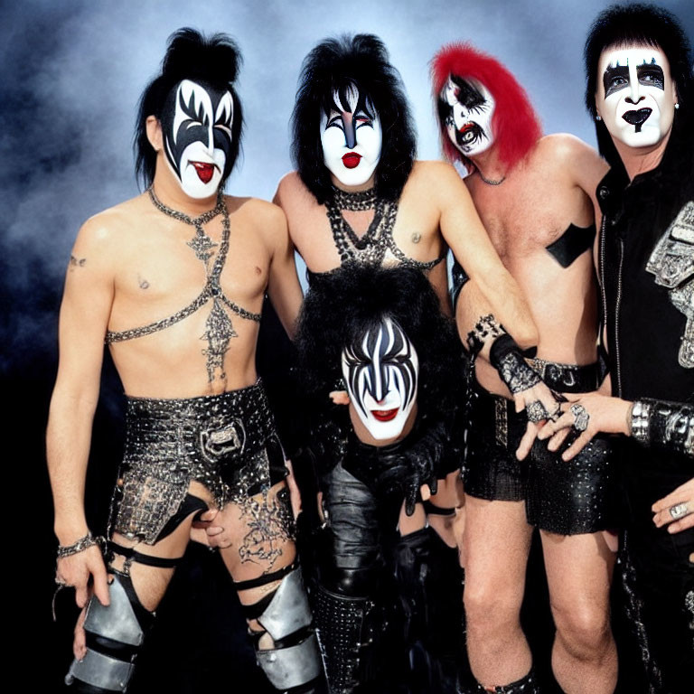 Four individuals in black and white face paint and rock outfits pose on smoky background