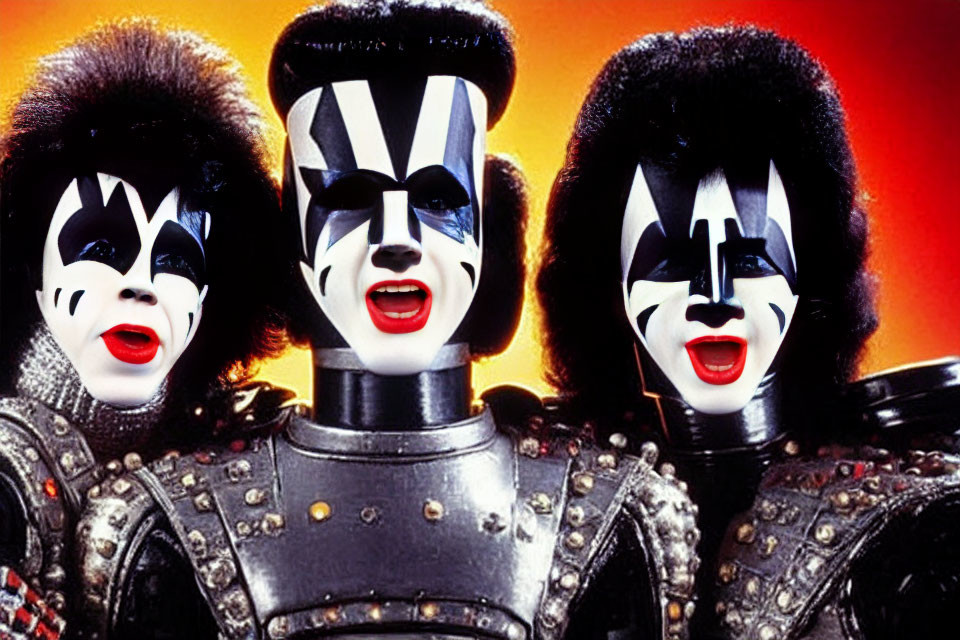 Three individuals in black and white face makeup and flamboyant rock costumes against fiery orange backdrop