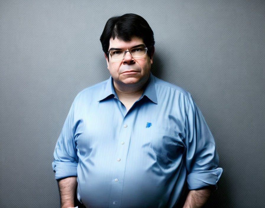 Man in Blue Shirt with Glasses Against Grey Backdrop