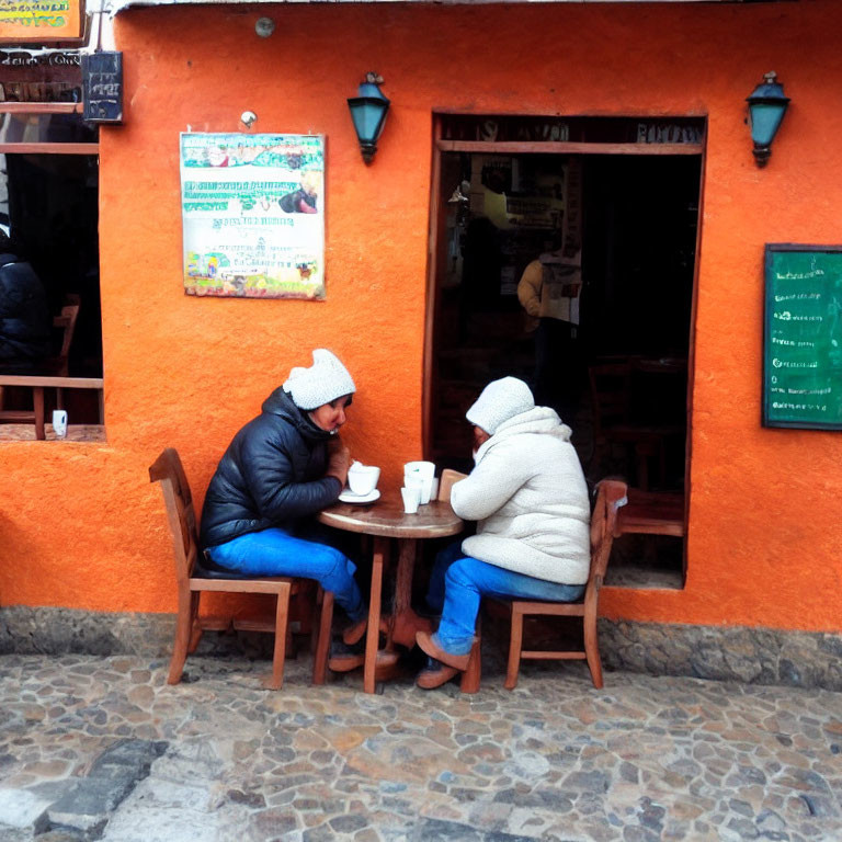 Two individuals at outdoor cafe table on cobblestone sidewalk