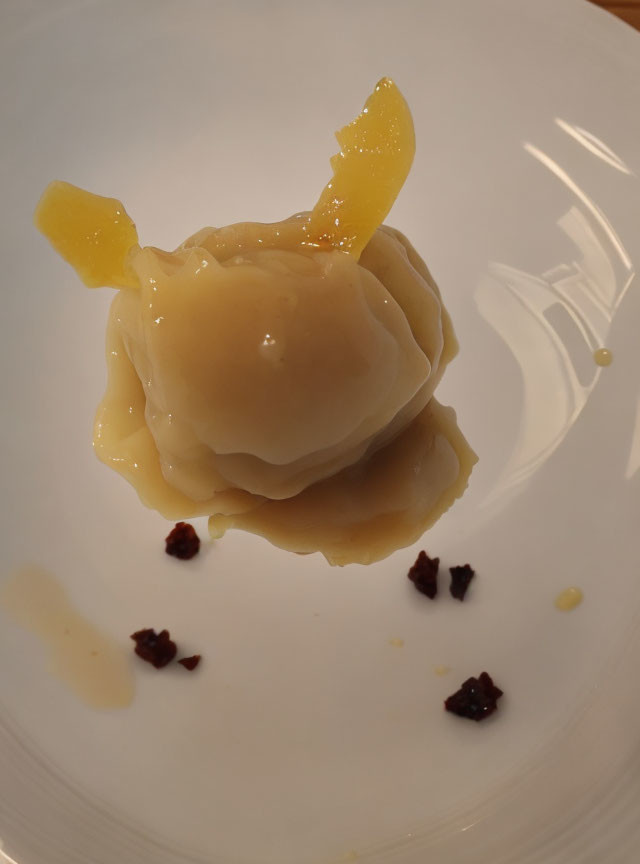 Plated dumpling with yellow fruit slices and sauce garnish