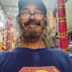 Smiling man with dreadlocks, beard, glasses, cartoon t-shirt, colorful background
