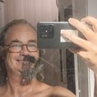 Person holding smartphone with curled mustache, mirrored reflection.