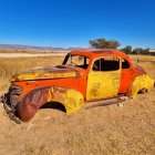 Customized vintage car with rust-like paint and flame decals in open field